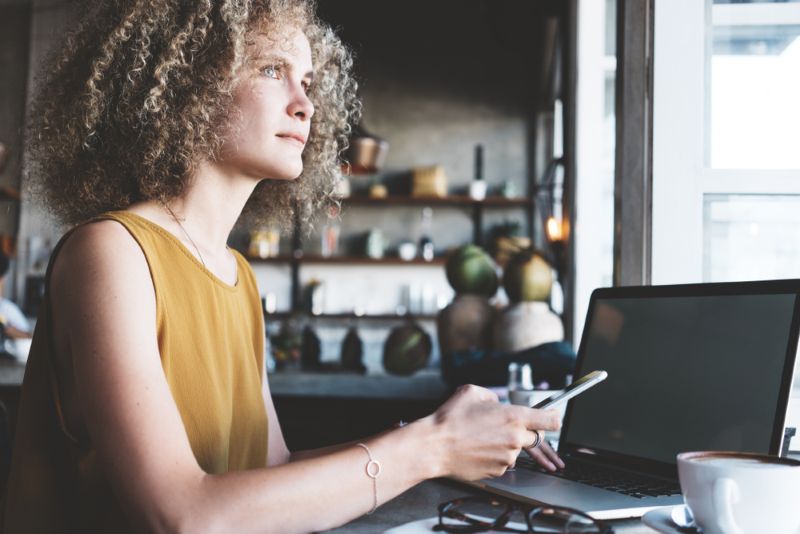 Woman using her cell phone while sitting in front of her laptop